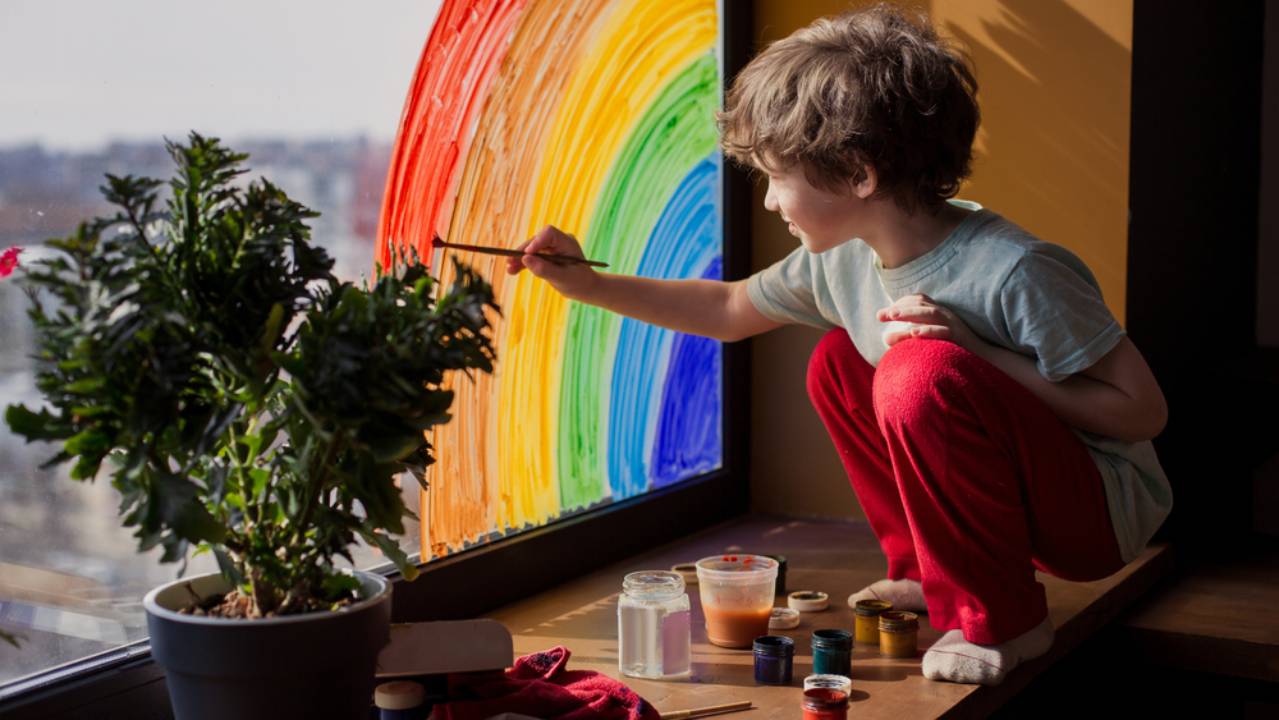 bambino che disegna arcobaleno su un vetro