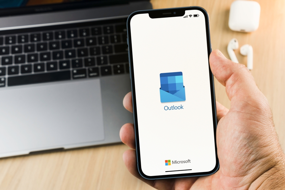 Avvio programma Outlook su smartphone con laptop sullo sfondo Avvio programma Outlook su smartphone con laptop sullo sfondo