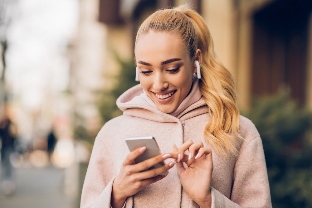 Ragazza sorridente con airpods e smartphone in mano Ragazza sorridente con airpods e smartphone in mano