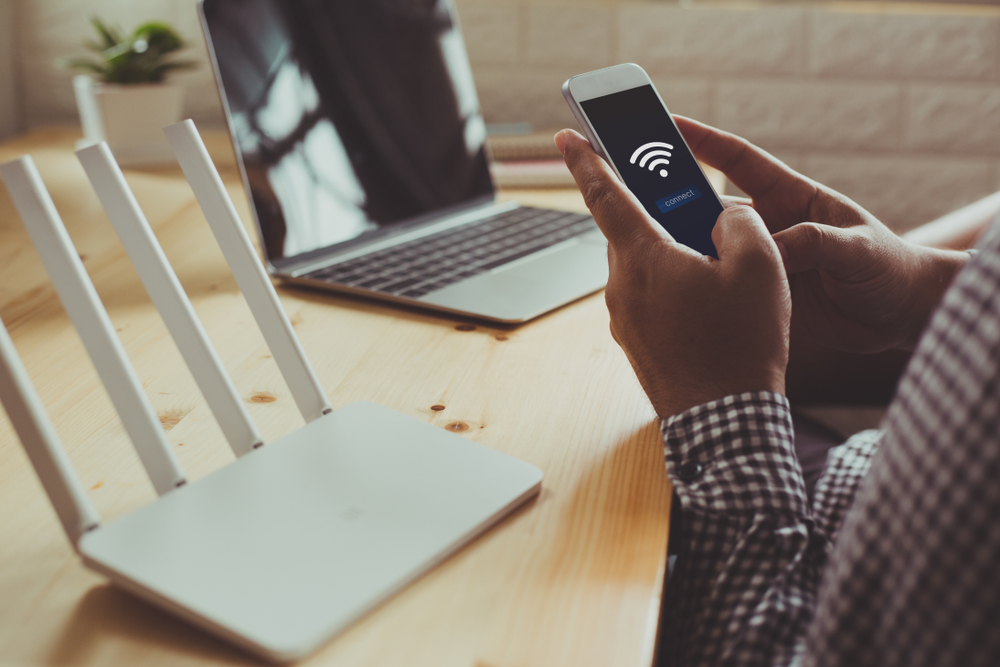 Smartphone in collegamento wifi con router e laptop sullo sfondo