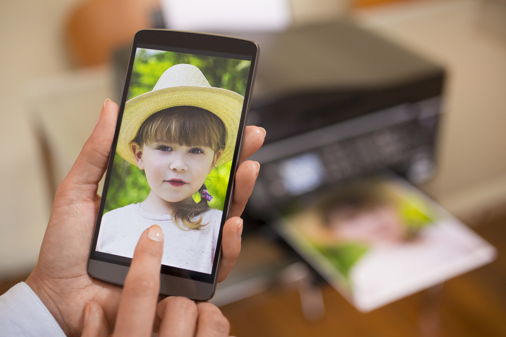 Foto di bambina sul cellulare con stampante sullo sfondo
