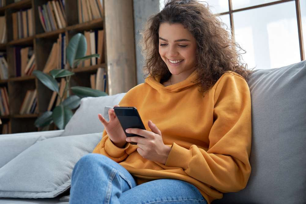 Ragazza sul divano con cellulare in mano Ragazza sul divano con cellulare in mano