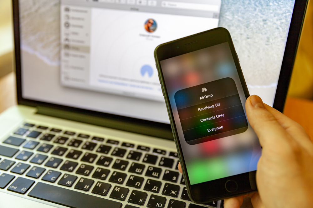 App AirDrop su iPhone con iMac sullo sfondo App AirDrop su iPhone con iMac sullo sfondo
